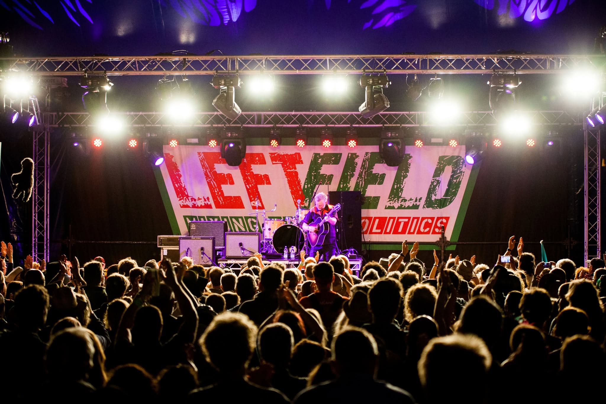 Billy Bragg performing on stage in front of a festival audience